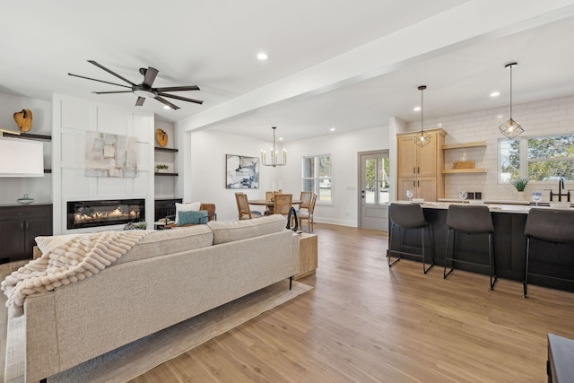 living area featuring recessed lighting, light wood-style floors, a large fireplace, baseboards, and ceiling fan with notable chandelier