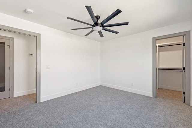 unfurnished bedroom with ceiling fan, carpet, baseboards, and a walk in closet