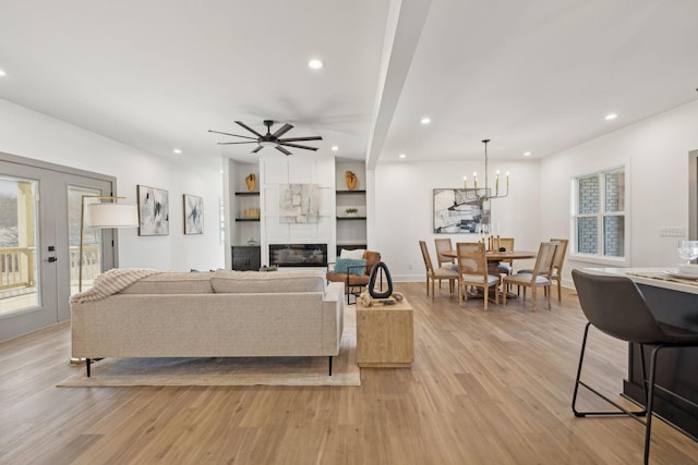 living room featuring light wood-type flooring, a large fireplace, ceiling fan with notable chandelier, and recessed lighting