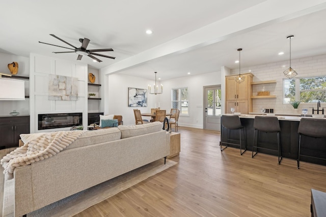 living area featuring recessed lighting, a large fireplace, ceiling fan with notable chandelier, baseboards, and light wood finished floors