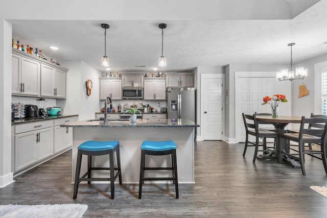 kitchen featuring hanging light fixtures, appliances with stainless steel finishes, a sink, an island with sink, and a kitchen breakfast bar