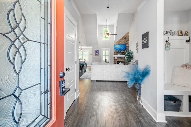 entrance foyer featuring ceiling fan, high vaulted ceiling, dark wood-style flooring, a fireplace, and baseboards