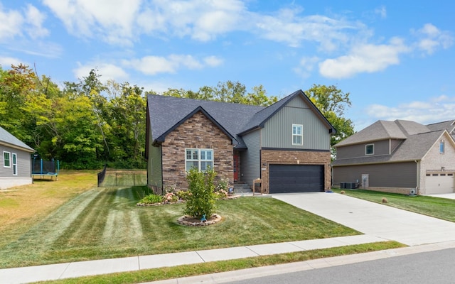 craftsman-style home featuring central air condition unit, a garage, concrete driveway, a trampoline, and a front yard