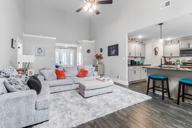 living area with dark wood-style floors, visible vents, a towering ceiling, ceiling fan, and baseboards