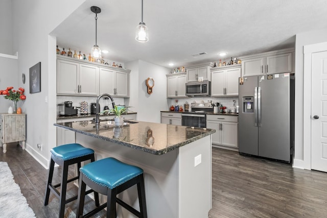 kitchen with a breakfast bar area, stainless steel appliances, hanging light fixtures, a sink, and an island with sink