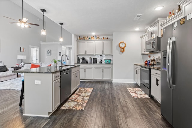 kitchen with a kitchen island with sink, stainless steel appliances, open floor plan, a kitchen bar, and dark wood finished floors