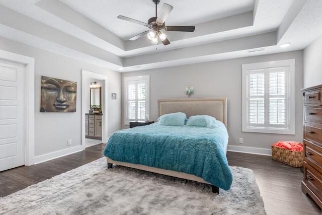 bedroom featuring dark wood-style floors, a tray ceiling, and multiple windows