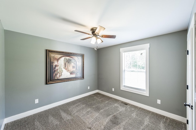 spare room featuring visible vents, dark carpet, a ceiling fan, and baseboards