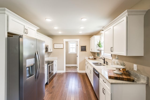 kitchen with dark wood-style flooring, stainless steel appliances, light countertops, white cabinetry, and a sink