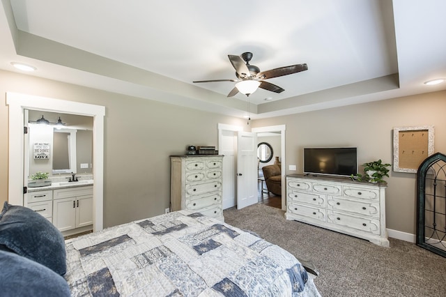 bedroom with a tray ceiling, carpet, connected bathroom, a sink, and baseboards