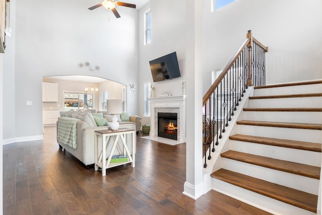 living area with baseboards, arched walkways, dark wood-type flooring, and ceiling fan with notable chandelier