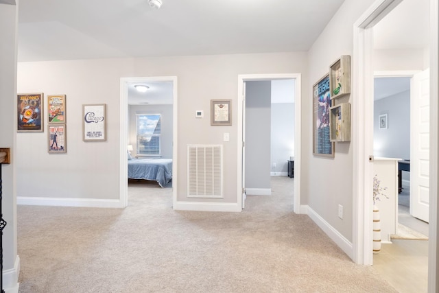 hallway featuring baseboards, visible vents, and light colored carpet