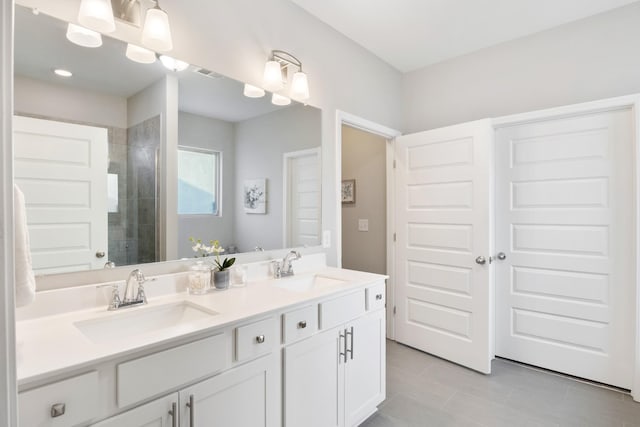 bathroom featuring a tile shower, double vanity, a sink, and visible vents