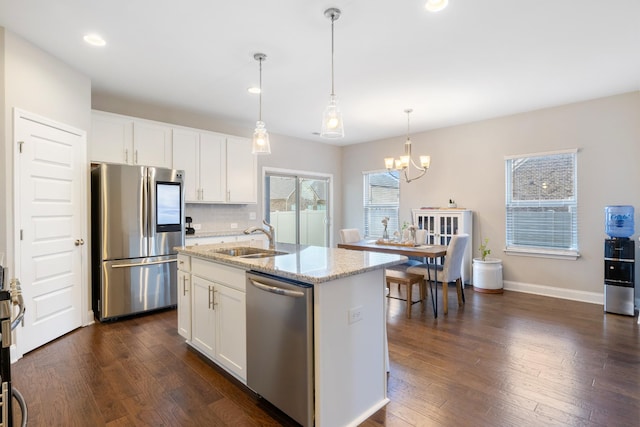 kitchen featuring light stone counters, a kitchen island with sink, stainless steel appliances, white cabinetry, and a sink