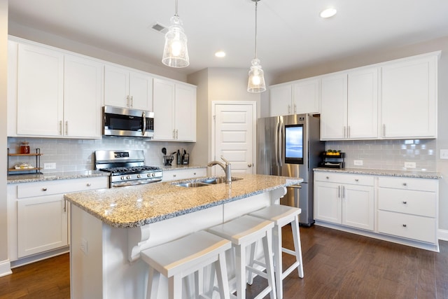 kitchen with a sink, visible vents, white cabinets, hanging light fixtures, and appliances with stainless steel finishes