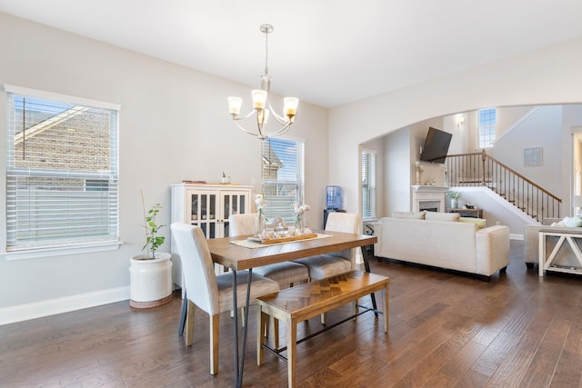 dining area with arched walkways, baseboards, dark wood-type flooring, a fireplace, and a chandelier