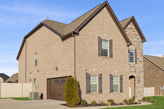 view of side of property featuring stone siding, concrete driveway, brick siding, and fence