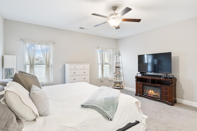 bedroom with visible vents, baseboards, a ceiling fan, a glass covered fireplace, and carpet