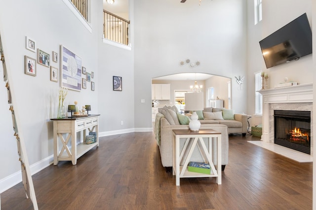 living area with baseboards, dark wood finished floors, arched walkways, a premium fireplace, and an inviting chandelier