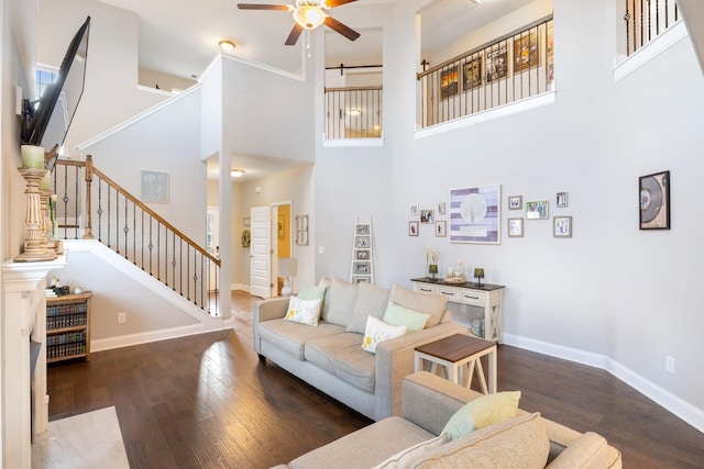 living area featuring baseboards, a ceiling fan, dark wood-style floors, a high ceiling, and stairs