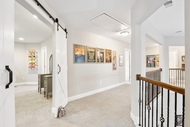 hallway featuring light carpet, baseboards, visible vents, and a barn door