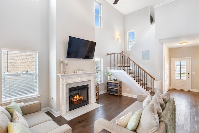 living room with dark wood-style floors, a towering ceiling, stairway, a premium fireplace, and baseboards