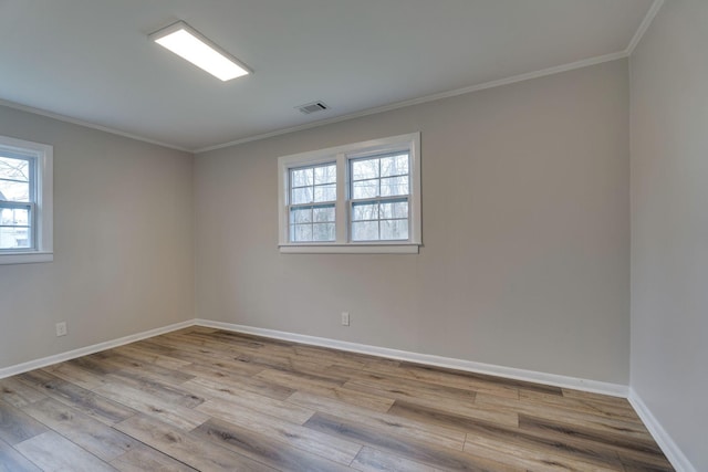 empty room featuring light wood-style floors, visible vents, crown molding, and baseboards