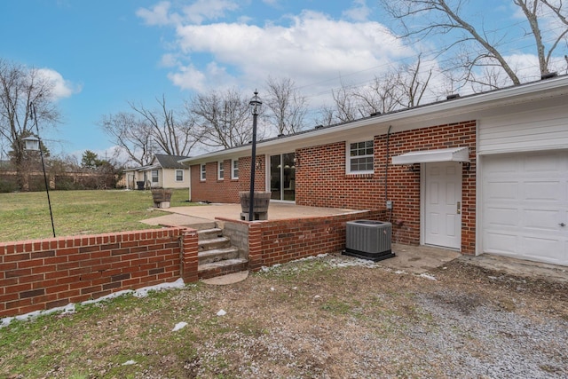 back of house with central AC unit, a lawn, an attached garage, a patio area, and brick siding