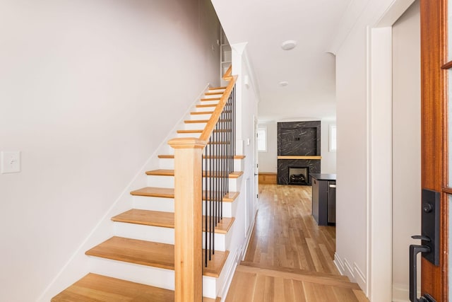 stairway with a premium fireplace, baseboards, and wood finished floors