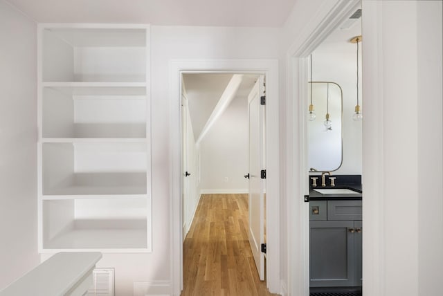 hall featuring light wood-type flooring, visible vents, and a sink