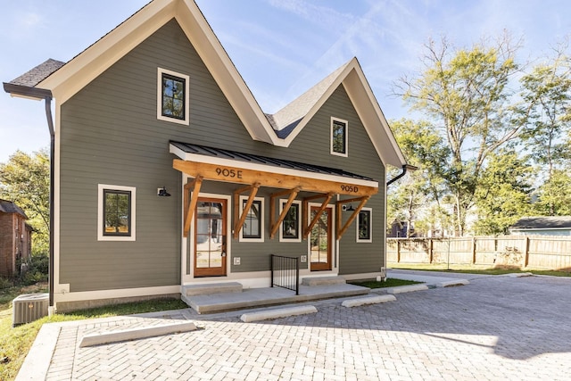 view of front facade featuring metal roof, cooling unit, covered porch, fence, and a standing seam roof