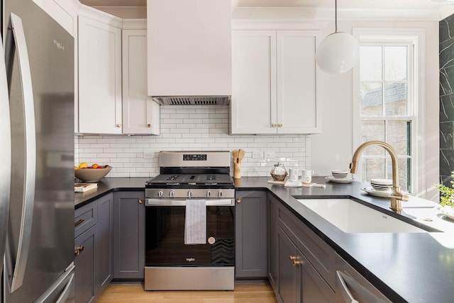 kitchen with dark countertops, gray cabinets, stainless steel appliances, white cabinetry, and a sink