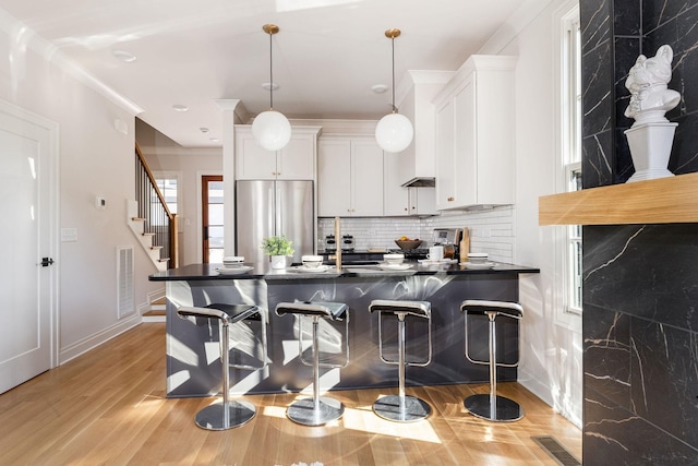 kitchen with pendant lighting, dark countertops, visible vents, freestanding refrigerator, and white cabinetry