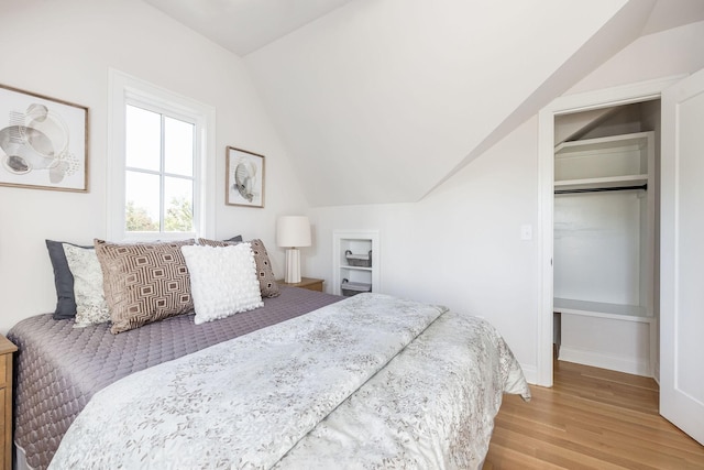 bedroom featuring lofted ceiling, light wood-style floors, baseboards, and a walk in closet