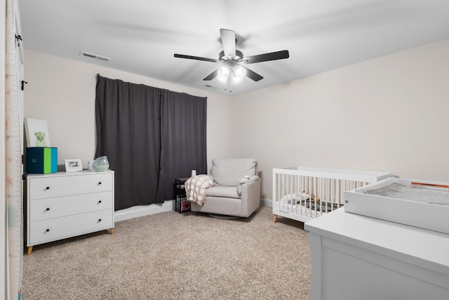 bedroom with a crib, light carpet, and a ceiling fan