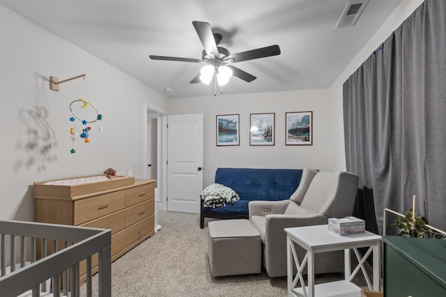 bedroom featuring light carpet, a nursery area, and a ceiling fan