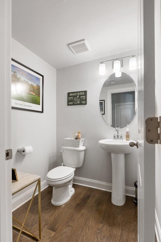 half bath featuring toilet, baseboards, visible vents, and wood finished floors