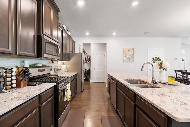 kitchen with stainless steel appliances, dark wood-type flooring, dark brown cabinetry, a sink, and an island with sink