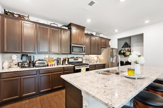 kitchen featuring a center island with sink, stainless steel appliances, visible vents, a sink, and a kitchen bar