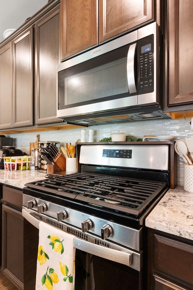 kitchen featuring stainless steel appliances, dark brown cabinetry, light stone counters, and tasteful backsplash