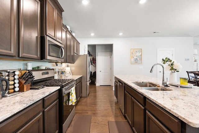 kitchen with light stone counters, recessed lighting, appliances with stainless steel finishes, dark wood-type flooring, and a sink