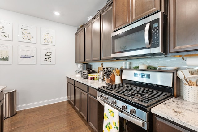 kitchen featuring stainless steel appliances, decorative backsplash, dark brown cabinetry, and light stone countertops