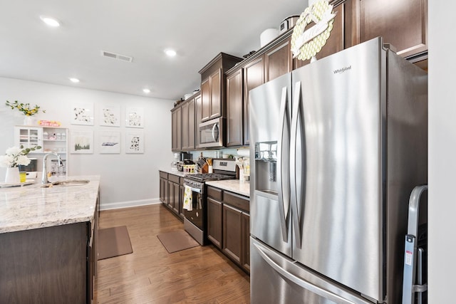 kitchen featuring dark brown cabinetry, appliances with stainless steel finishes, light stone counters, and a sink