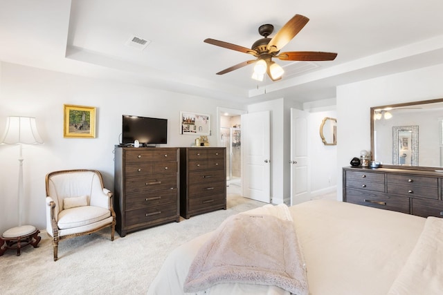 bedroom featuring ceiling fan, light colored carpet, visible vents, a tray ceiling, and ensuite bath