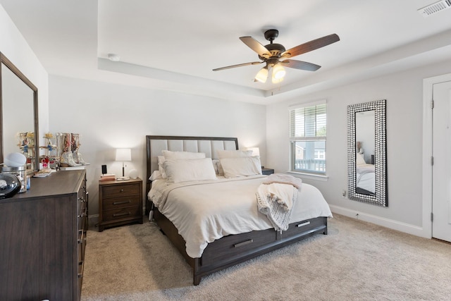 bedroom featuring ceiling fan, light carpet, visible vents, baseboards, and a tray ceiling