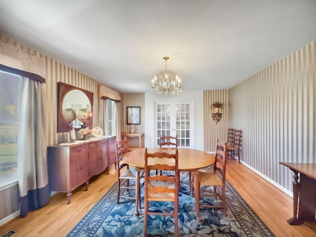 dining space with wallpapered walls, baseboards, french doors, light wood-style floors, and a chandelier