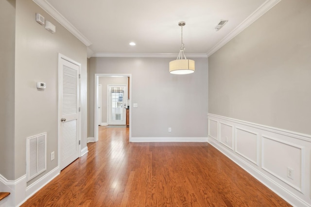 unfurnished dining area with visible vents, a decorative wall, wood finished floors, and ornamental molding