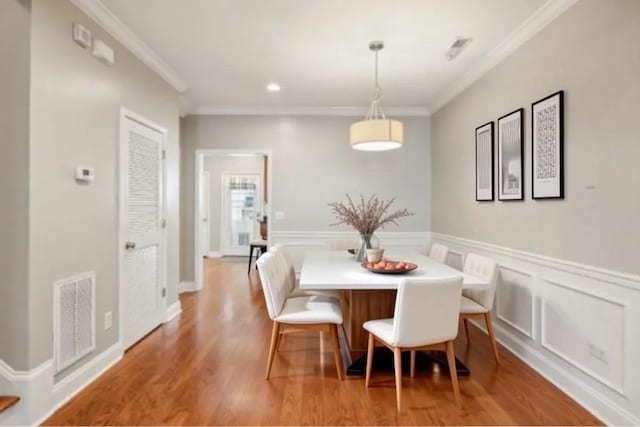 dining area with ornamental molding, light wood-style flooring, wainscoting, and visible vents