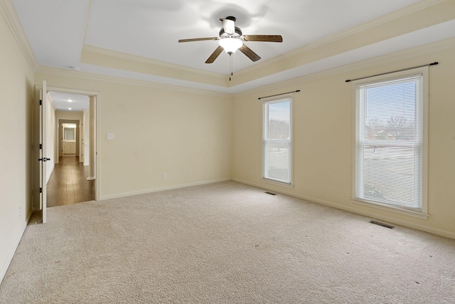 empty room featuring baseboards, a raised ceiling, a ceiling fan, ornamental molding, and carpet