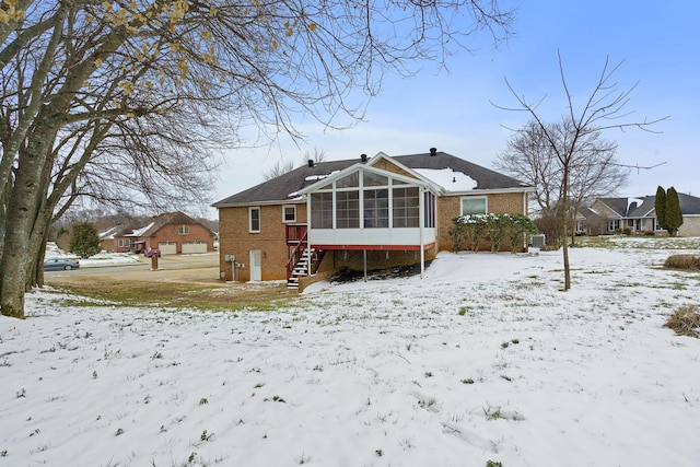 snow covered house featuring a sunroom and brick siding